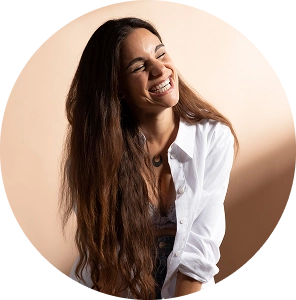 Vrouw met lang bruin haar lacht terwijl ze opzij kijkt, tegen een neutrale achtergrond.